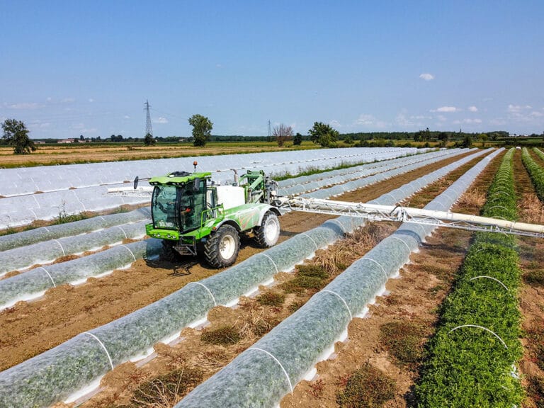 Trattore con braccio esteso in azione su serre tunnel per il trattamento e la cura delle colture